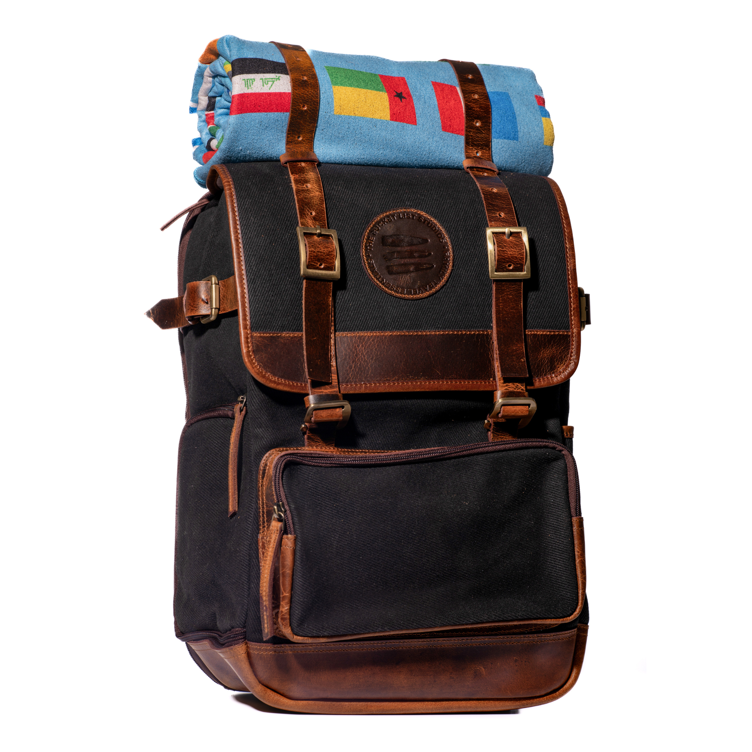 Product photo of a black canvas and leather backpack with a light blue rolltop blanket on top of the bag.