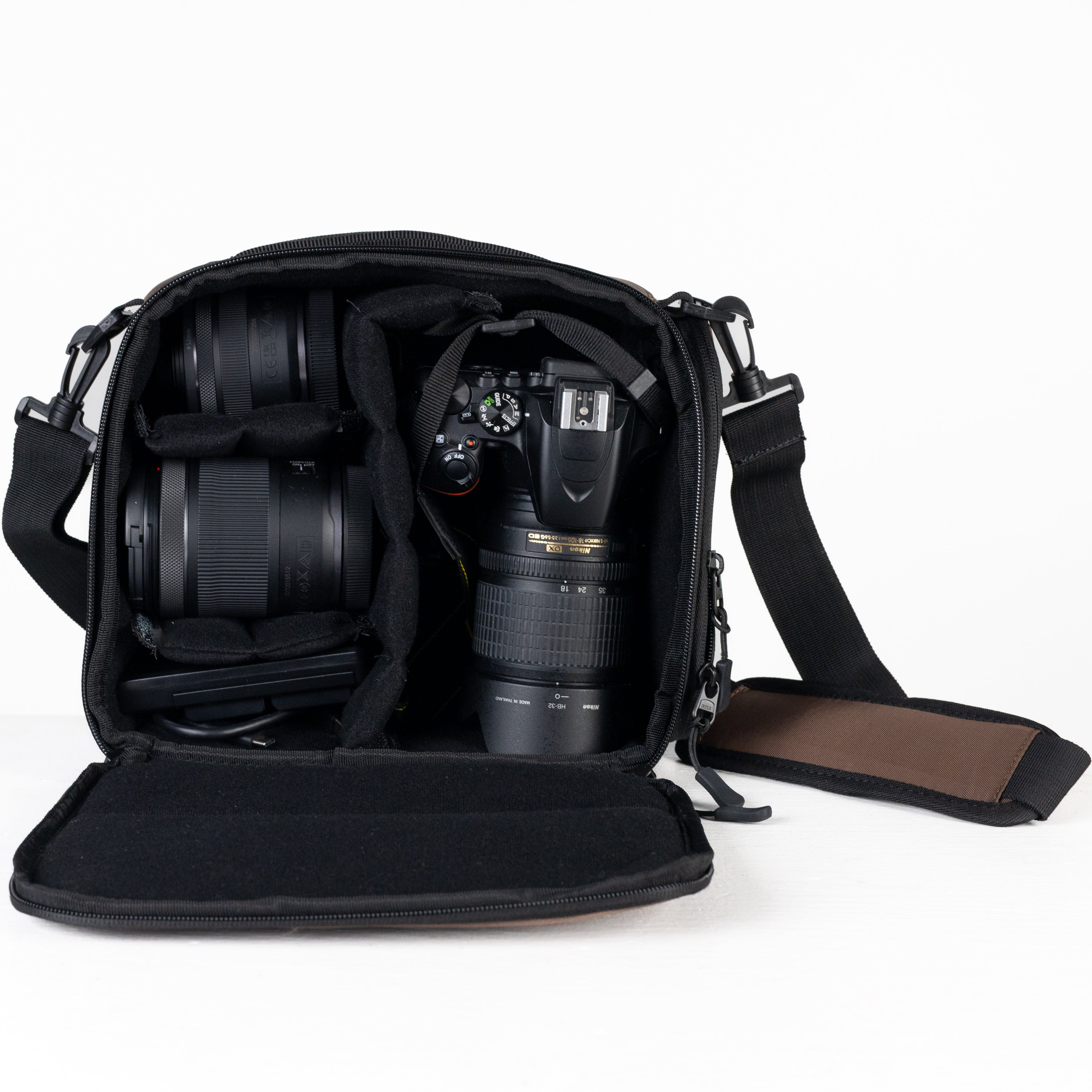 Product photo of a camera cube bag open on a white table with a white background. The bag has a black interior with a few compartments full of a camera and a few lenses.