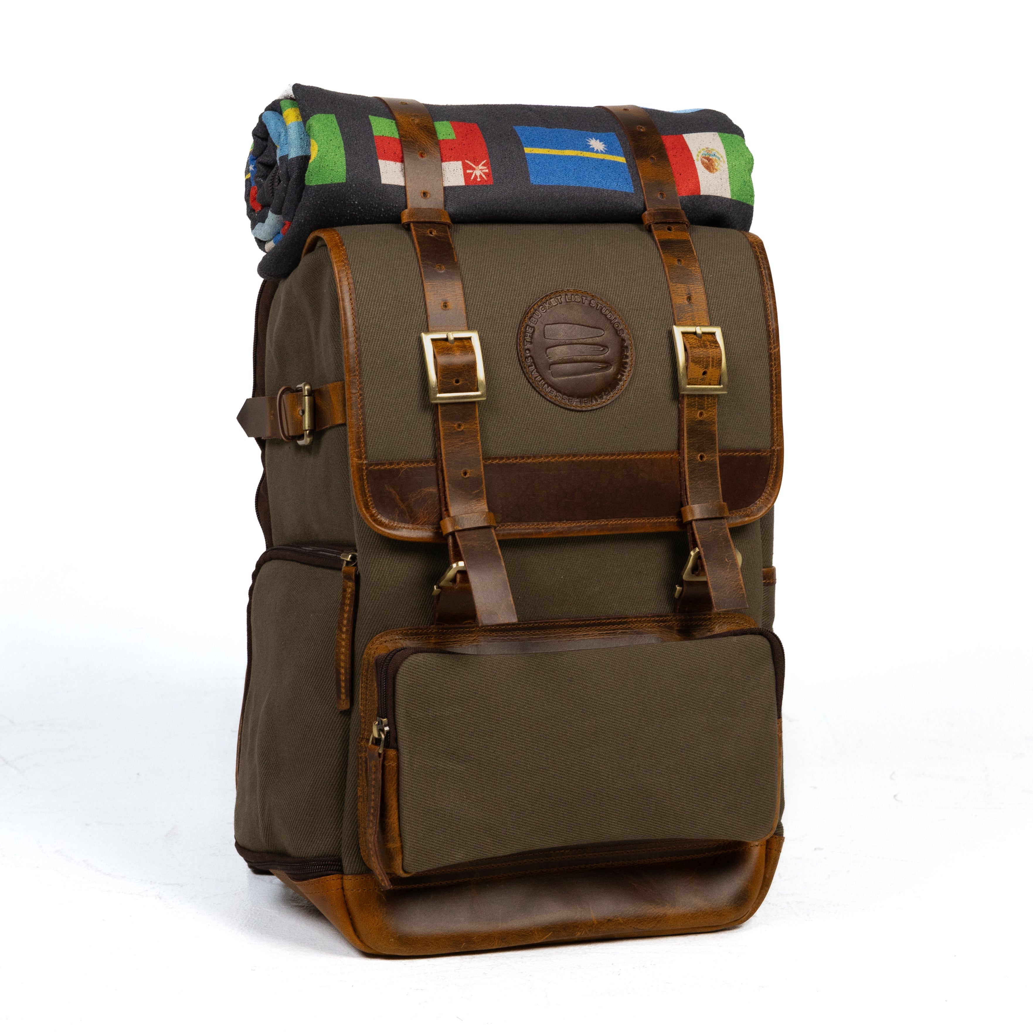 Product photo of a large vintage sage canvas and leather backpack with a black rolltop blanket on top of the bag.