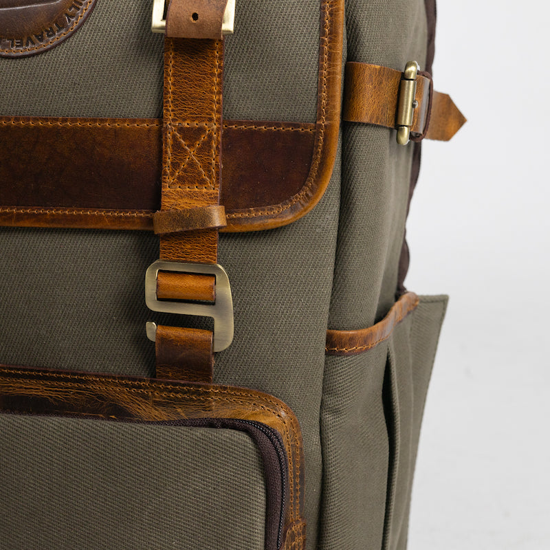 A close-up product photo of a metal hook on a vintage sage canvas and leather backpack.