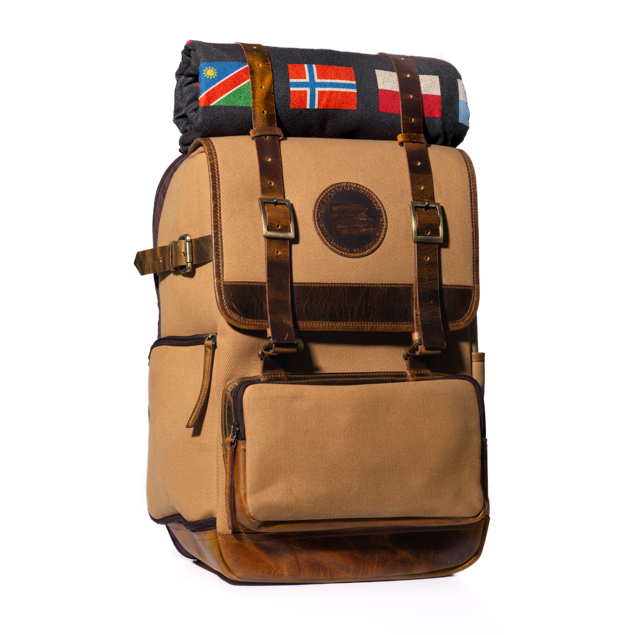 Product photo of a large tan canvas and leather backpack with a black rolltop blanket on top of the backpack.