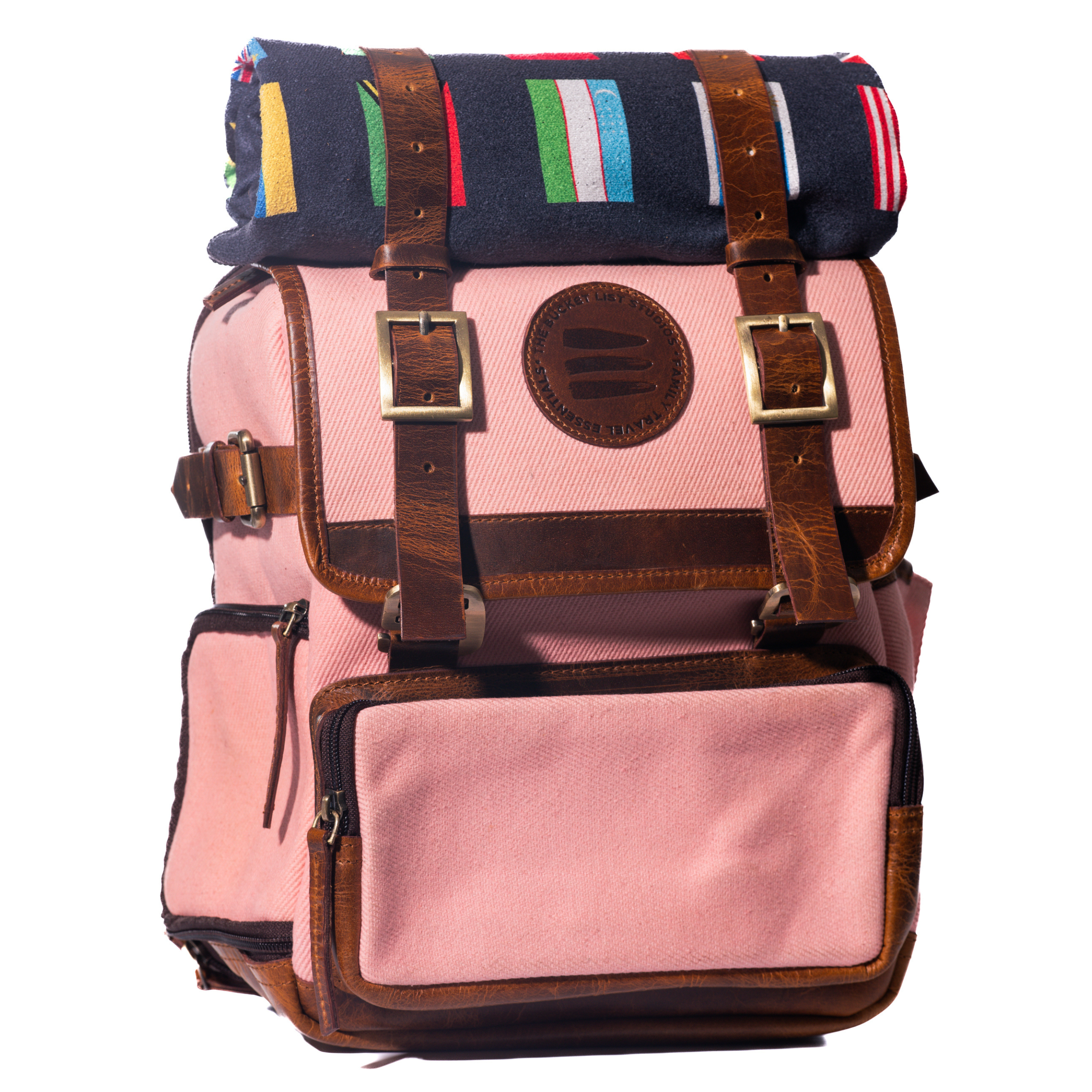 Product photo of a pink canvas and leather backpack with a black rolltop blanket on top of the backpack.