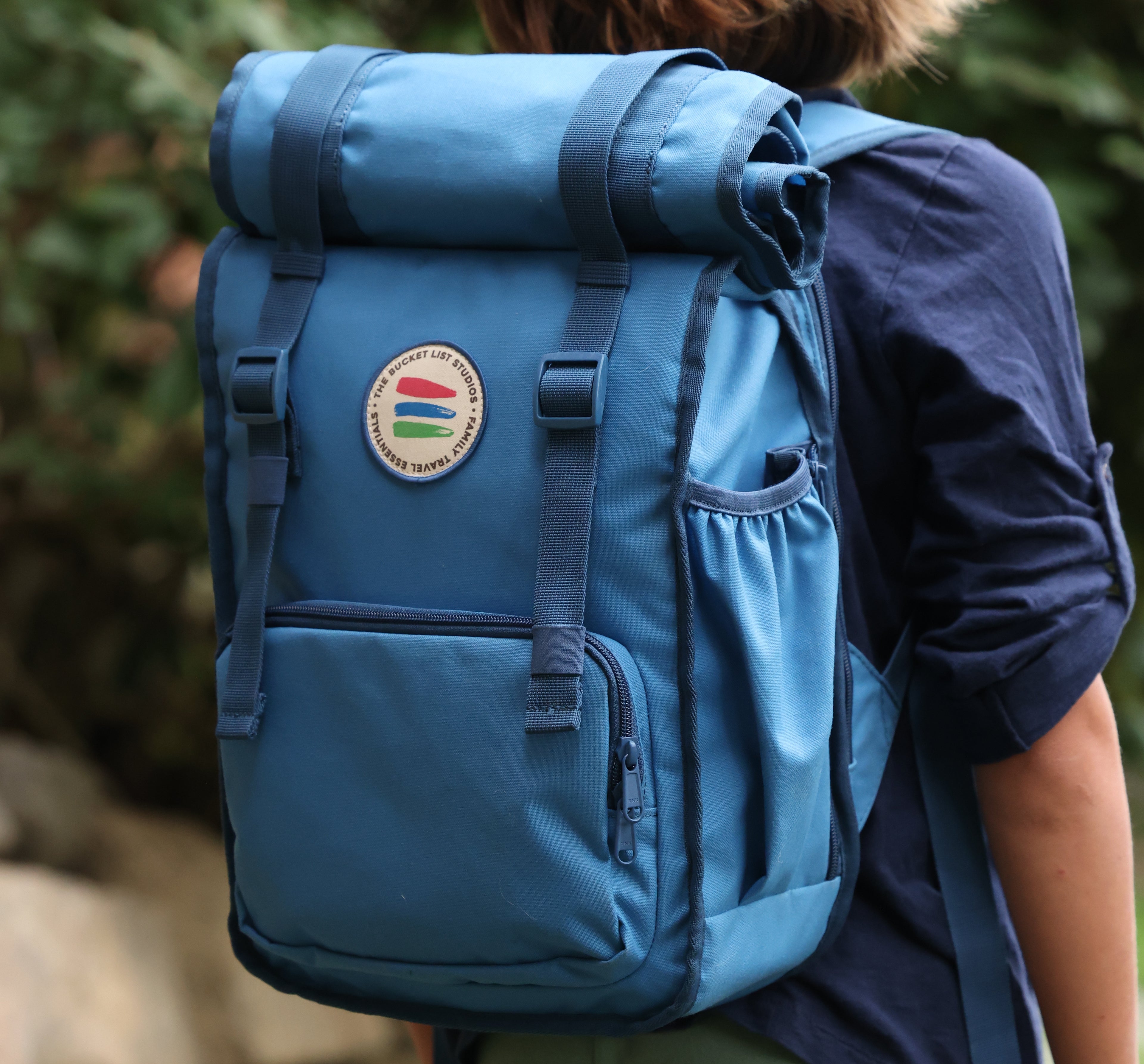 Blue backpack with a logo on a person's back against a blurred natural background