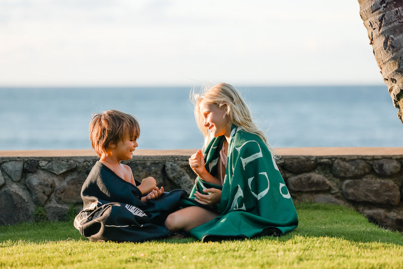 Two children playing rock, paper, scissors with each other on a lawn. They each have a blanket wrapped around them.