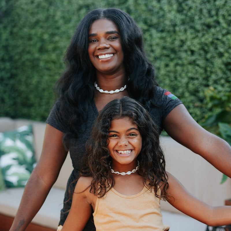 A photo of a mother and daughter wearing strung white shell necklaces.