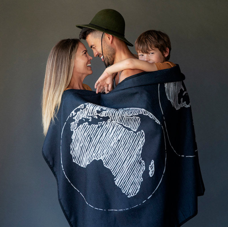 Studio photo of a family of three with a black blanket draped around them. The blanket has a white globe drawing on it.
