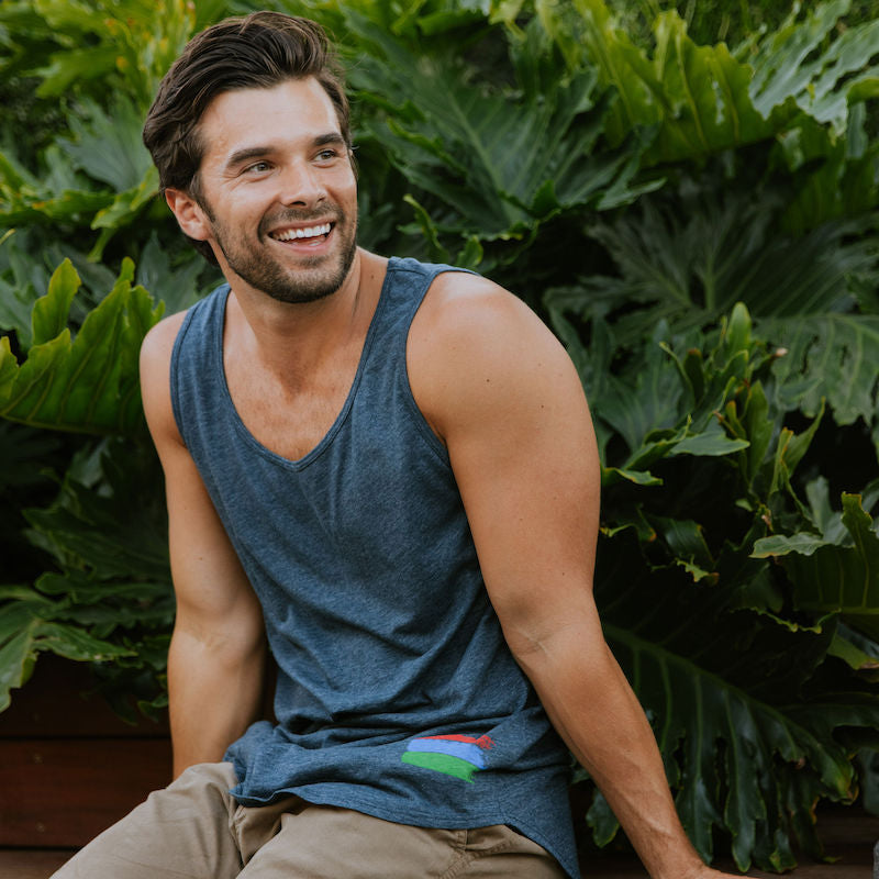 Photo of a man in a navy tank top sitting in front of a background of foliage.
