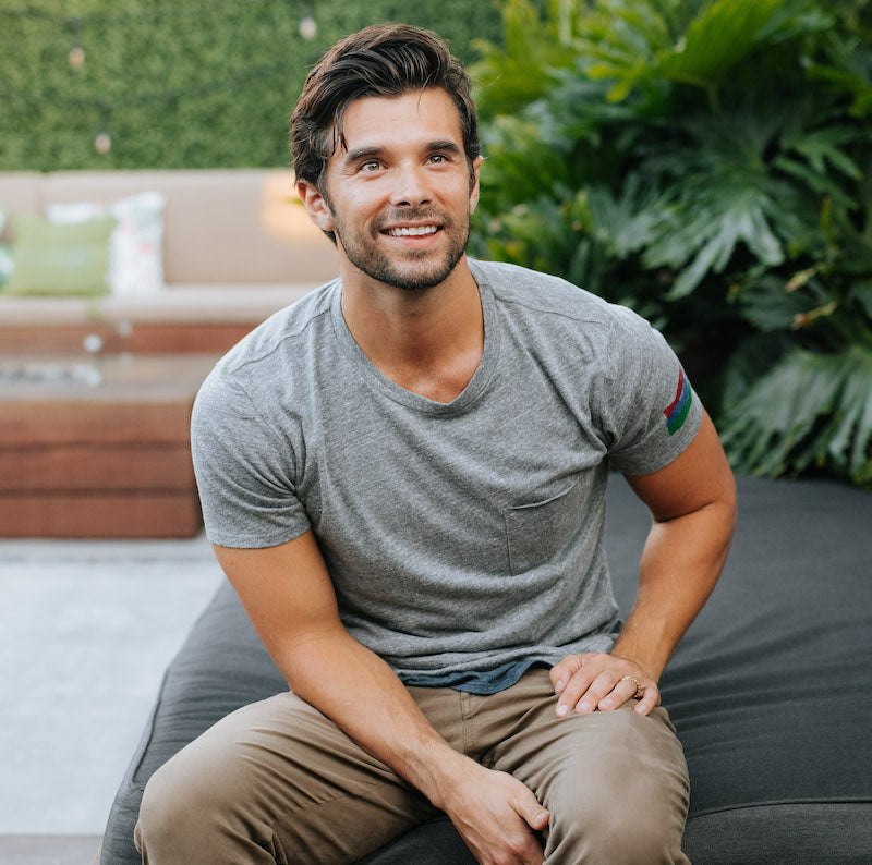 Photo of a man sitting on an outdoor ottoman wearing a grey t-shirt with a front pocket.