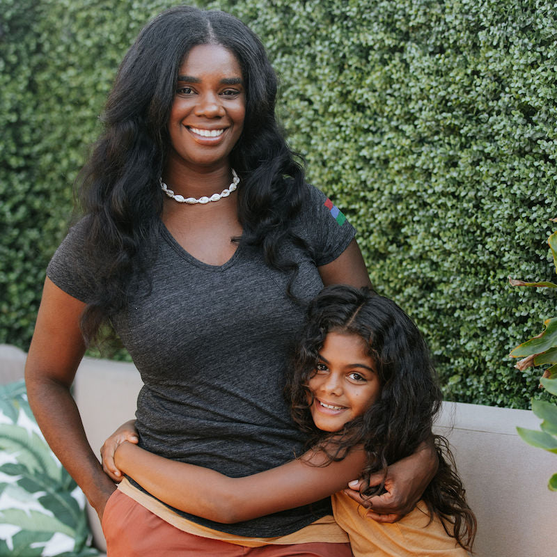 Photo of a mother and her daughter in front of a hedge. The mother is wearing a black v-neck short-sleeve t-shirt.