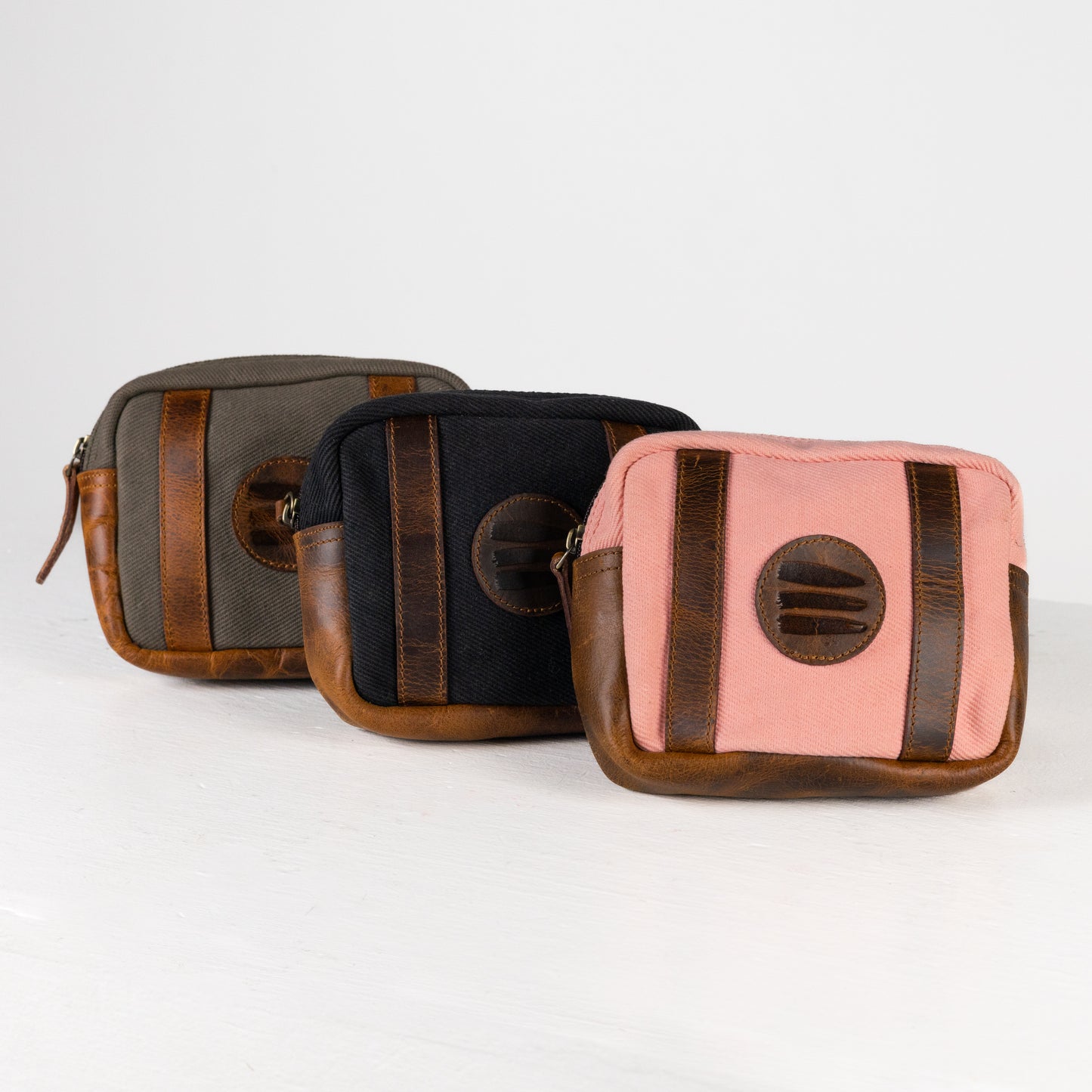 A product photo with vintage sage, black, and pink canvas and leather fanny packs all lined up on a white surface with a white background.