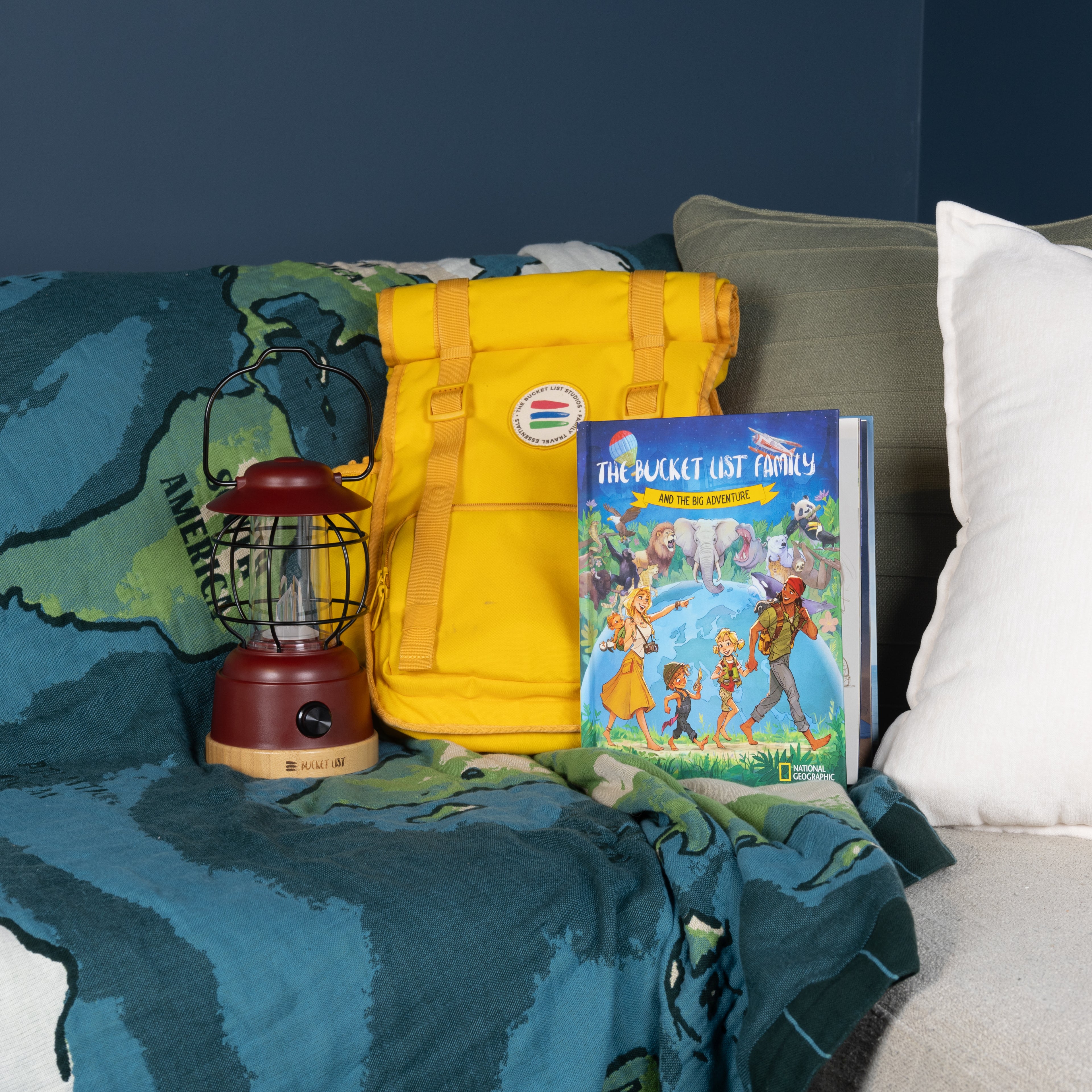 Yellow backpack, red lantern, and children's book on a couch with a world map blanket