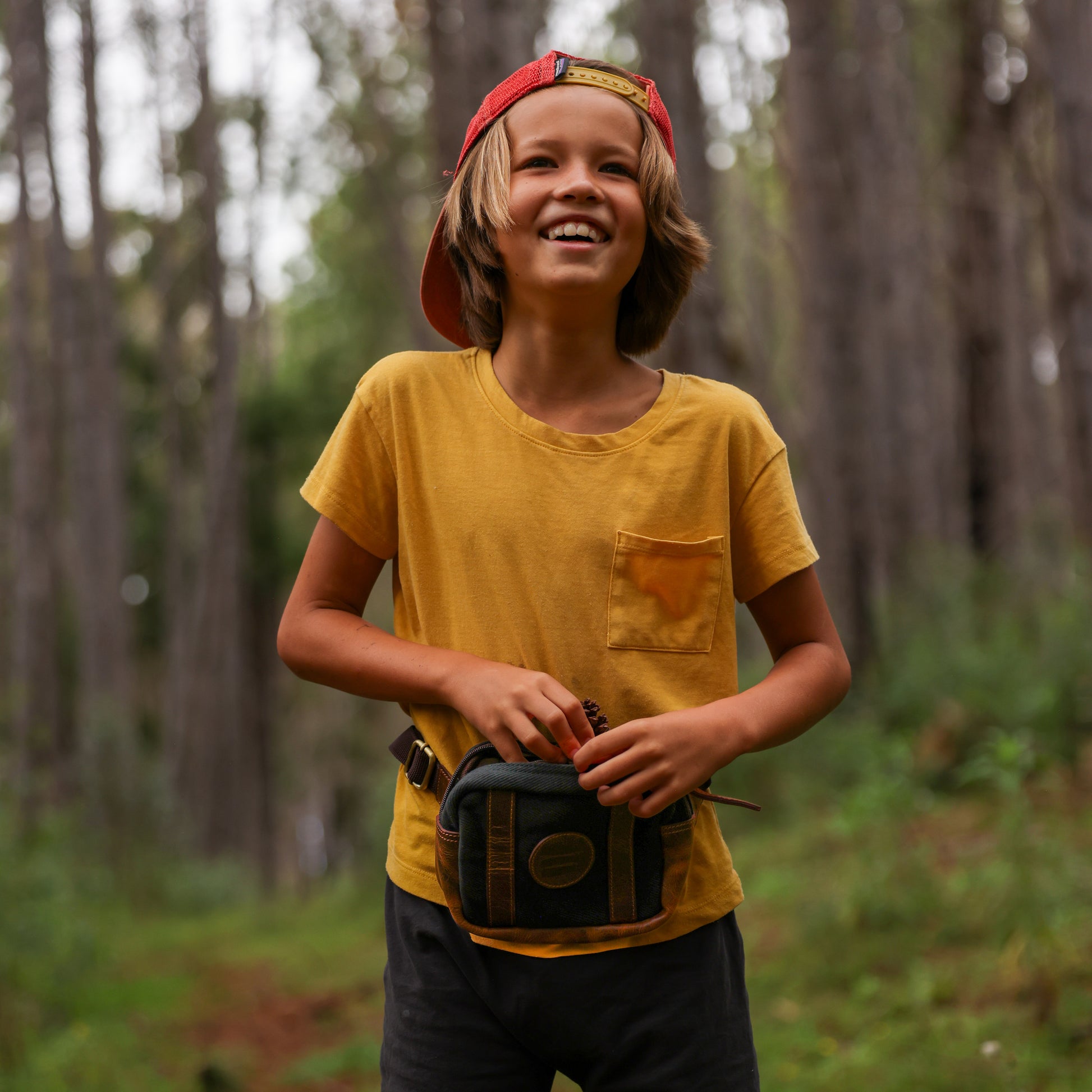 Photo of a boy in the woods wearing a yellow shirt and a black canvas and leather fanny pack around his waist.