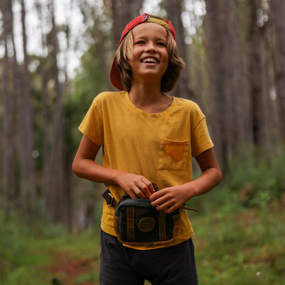 Photo of a boy in the woods wearing a yellow shirt and a black canvas and leather fanny pack around his waist.