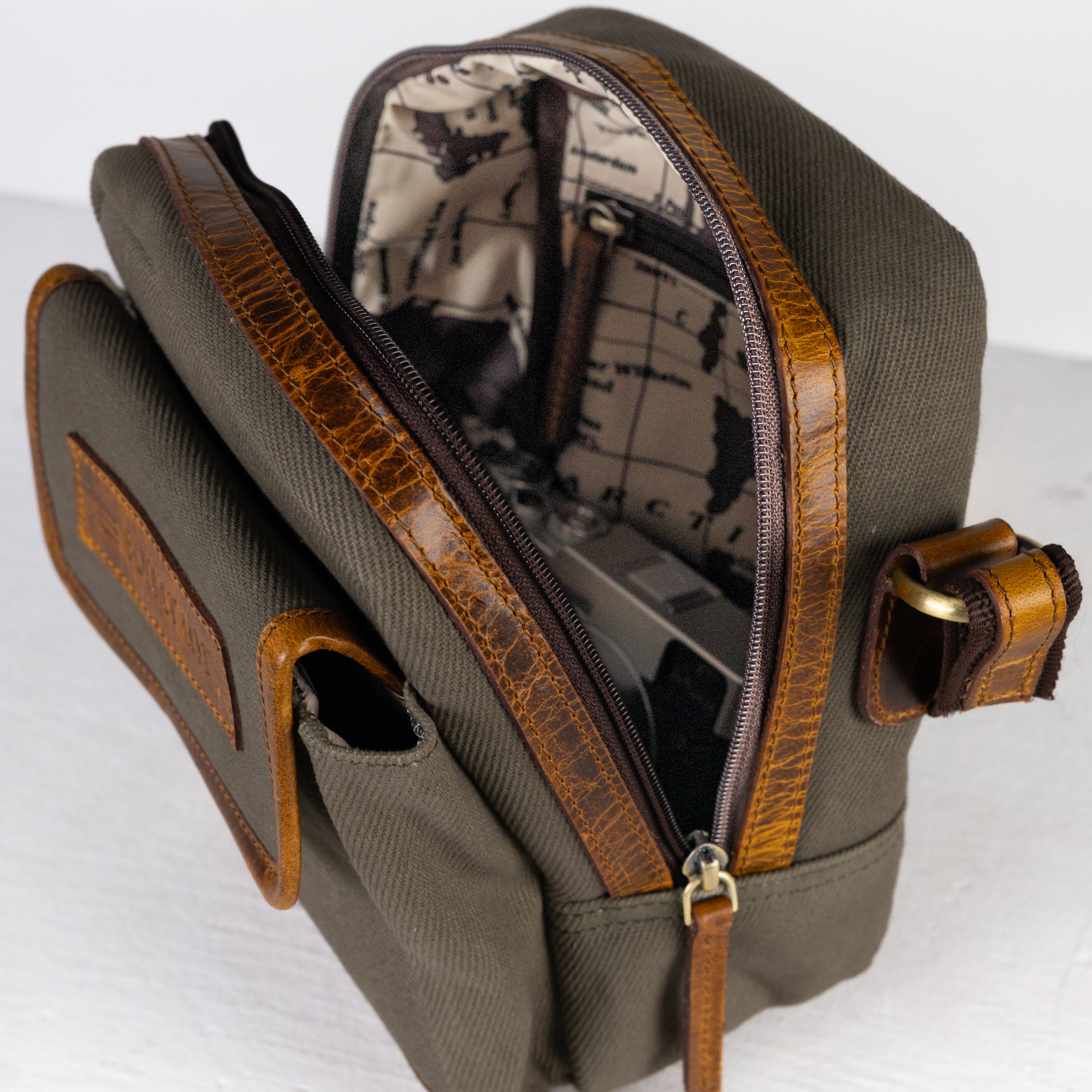 Product photo of a vintage sage canvas and leather side bag that is opened up on a table to show the inside.