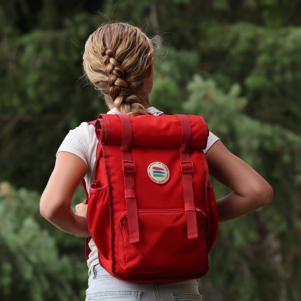 Person wearing a red backpack with a blurred green forest background