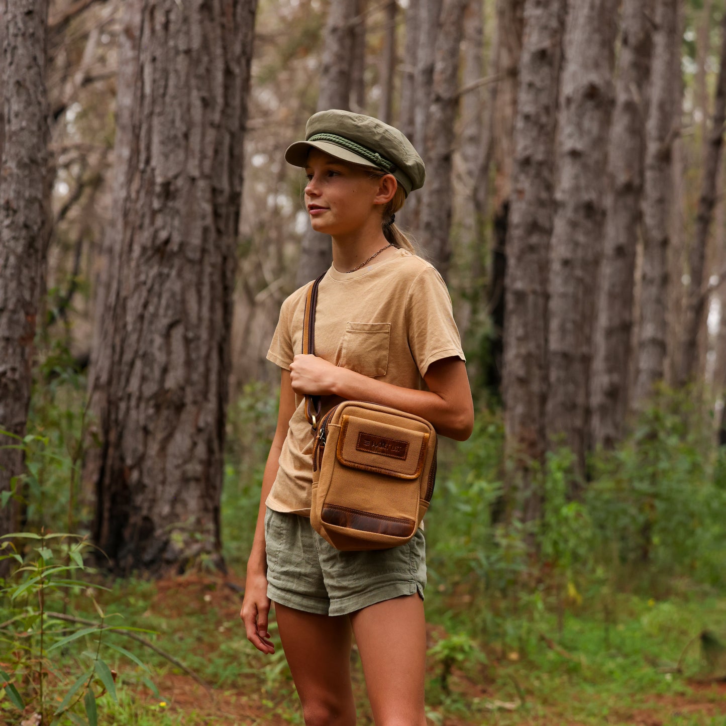 Photo of a girl wearing a tan sling pouch and standing in the woods.