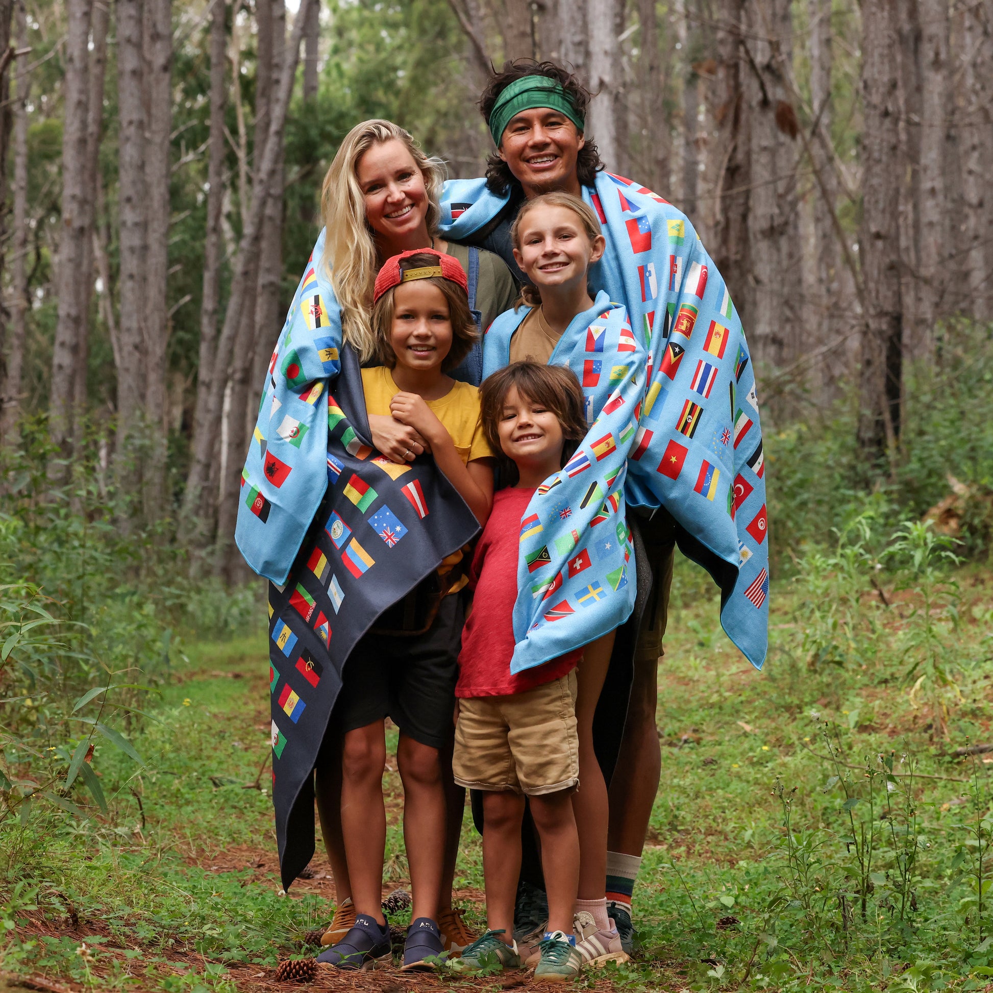 Photo of a family of five wrapped in two outdoor blankets. They're standing in the woods.