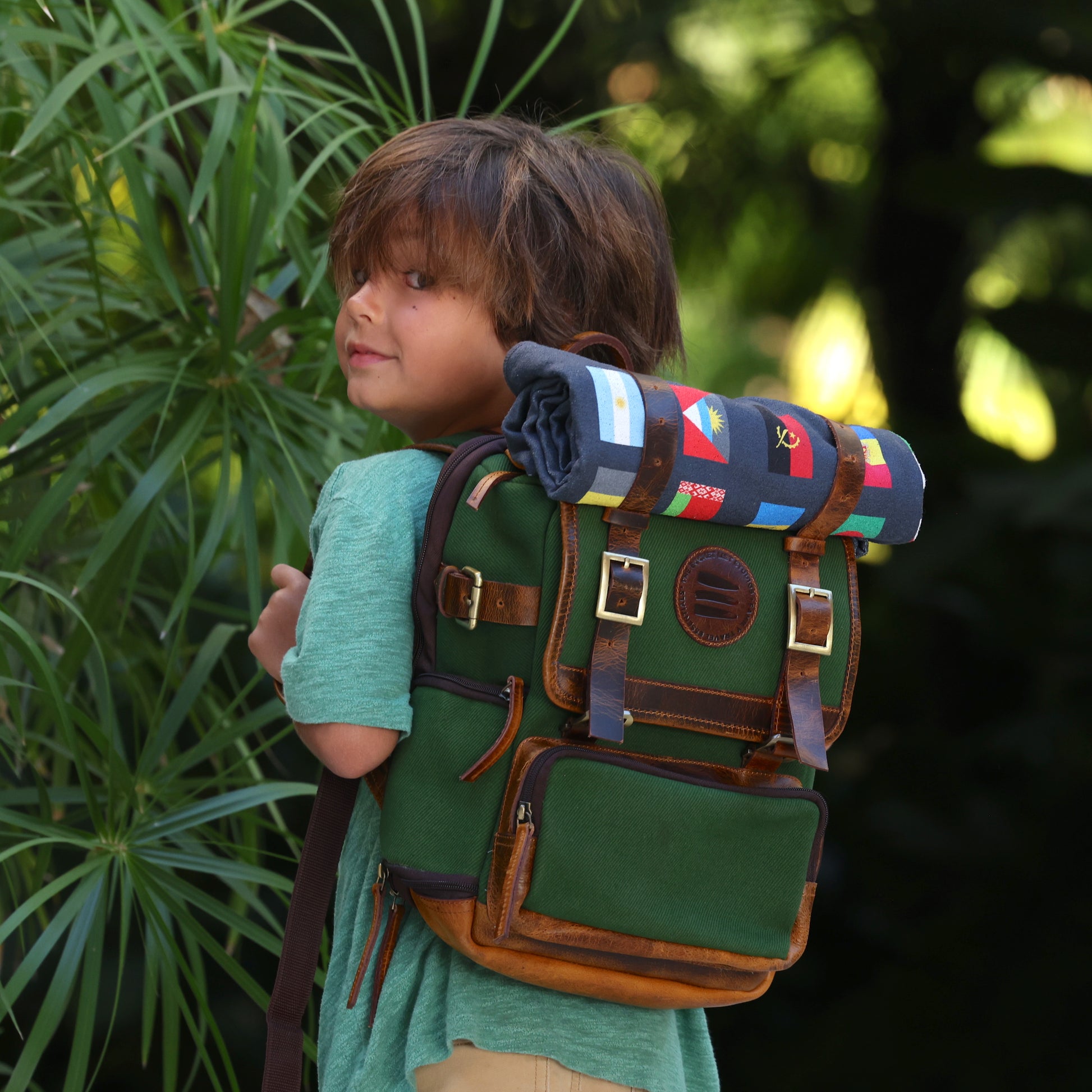 Photo of a boy looking back over his shoulder wearing a green canvas and leather backpack. 