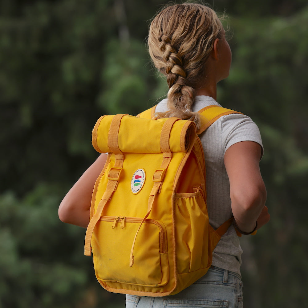 Person wearing a yellow backpack with a blurred green background