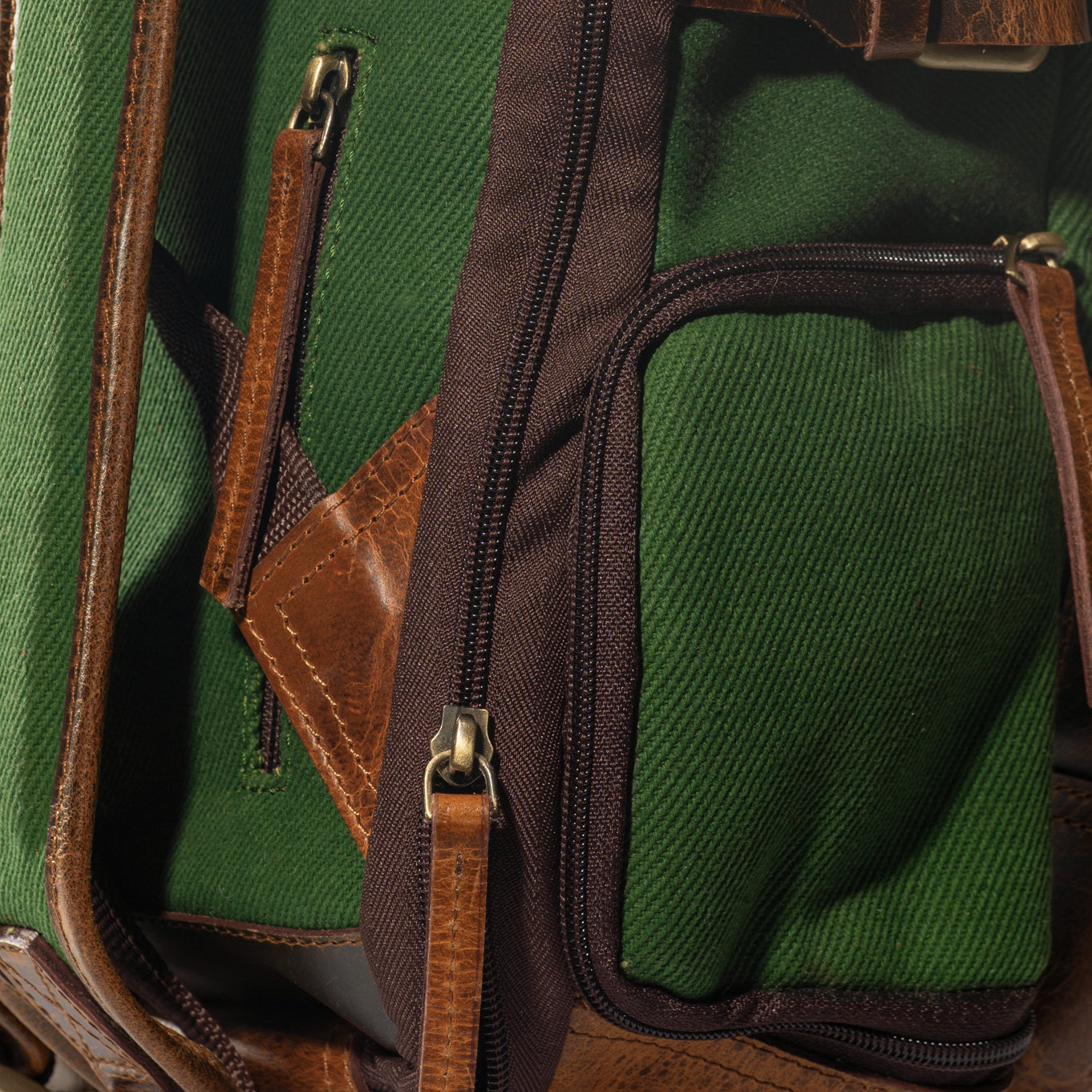 A close-up product photo of the zipper pocket of a green canvas and leather backpack.