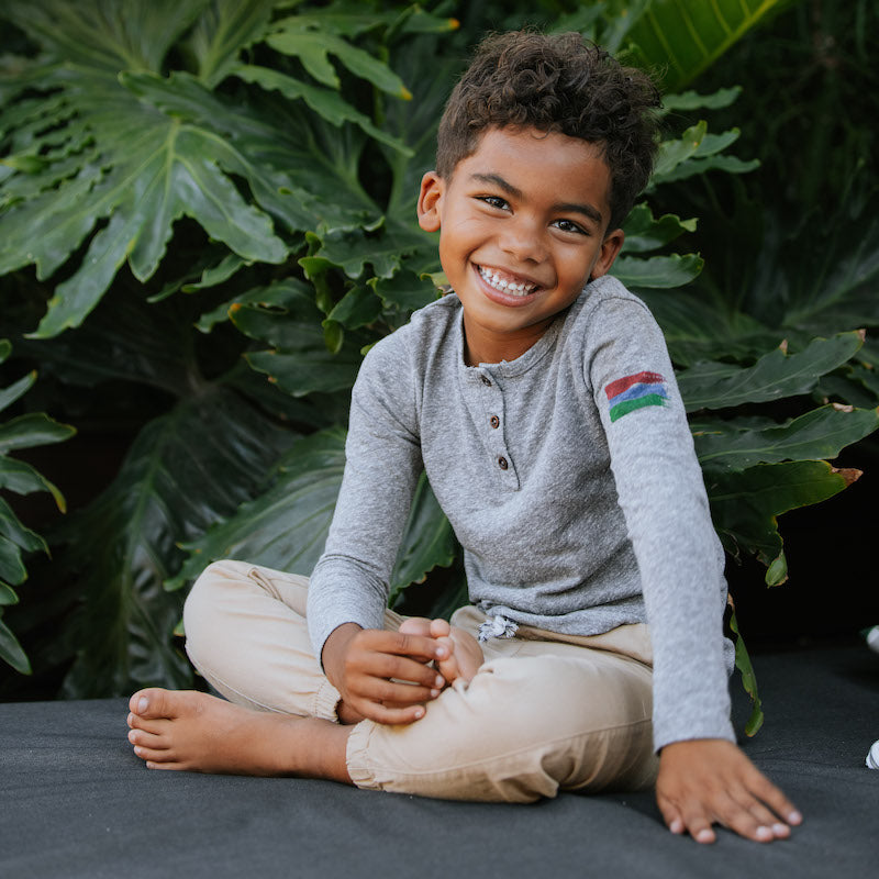 Photo of a young boy sitting down and wearing a grey henley. 