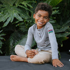 Photo of a young boy sitting down and wearing a grey henley. 