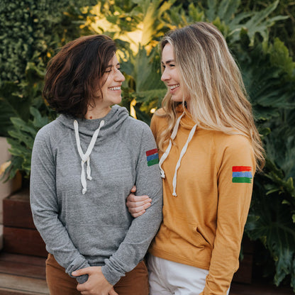 Photo of two women wearing a grey and a yellow hoodie looking at each other and smiling.