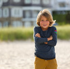 Photo of a young boy standing on a beach wearing a navy henley. 