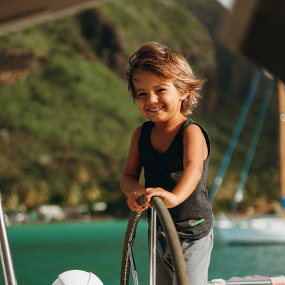 Picture of a young boy steering a sailboat wearing a black tank top and smiling at the camera.