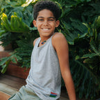 Picture of a boy wearing a grey tank top, sitting in front of a background of foliage.