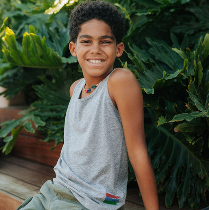 Picture of a boy wearing a grey tank top, sitting in front of a background of foliage.