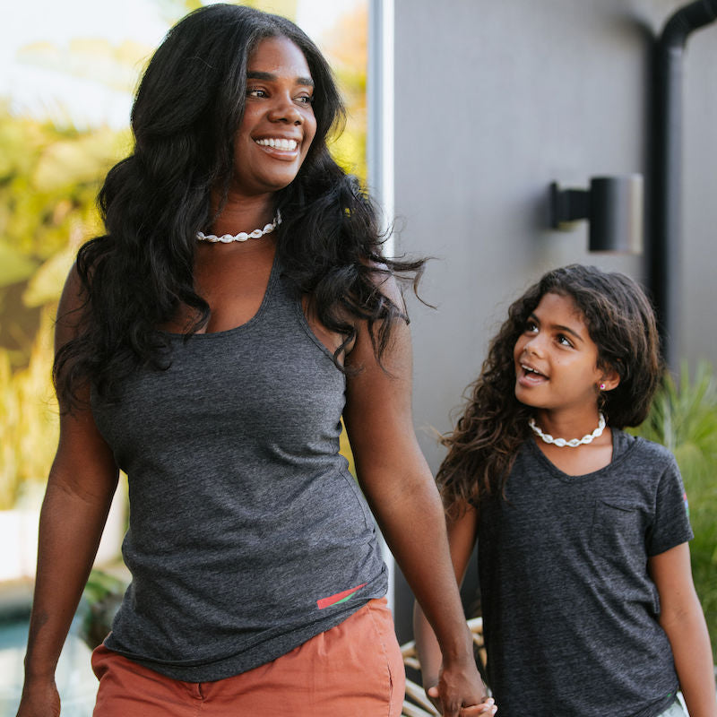 Photo of a mother and daughter holding hands. The mother is wearing a black tank top and the daughter is in a black t-shirt. 